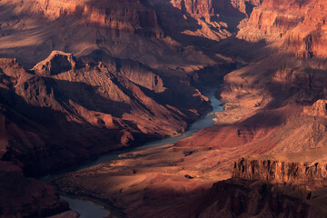 The Colorado River cuts through the bottom of the Grand Canyon in Arizona, USA on a bright sunny day during sunset.