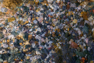 Rocky bottom of mountain stream, close-up. Colorful stones under clear water. Beautiful distortion background. Natural mosaic of small stones. Image for ceramic tile design, bathrooms.