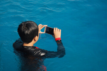 Asian boy using smartphone in the swimming pool. Technology, summer and holiday concept