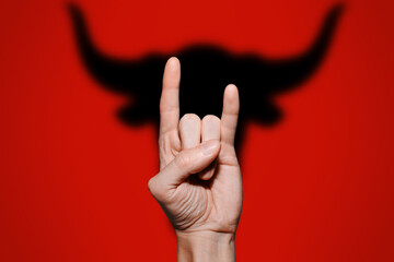 Male hand shows the gesture of a goat. Shadow in the form of a Bull, on a red background. Traditional Holiday Concept, Happy New Year 2021, Astrological Year of the Ox.