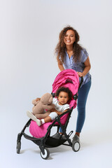 African-American woman and her cute baby in stroller on light background