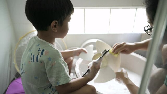Asian boy about 4 years old help his mother washing and cleaning dirty fan with brush