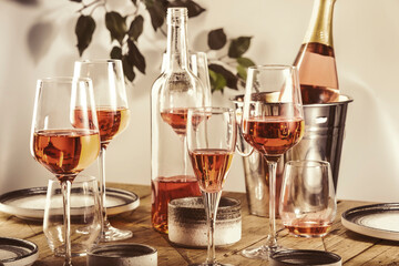 Rose wine glasses and bottles on table served for festive dinner party with different kinds of appetizers and fruits