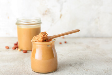 Jar and spoon with tasty peanut butter on table