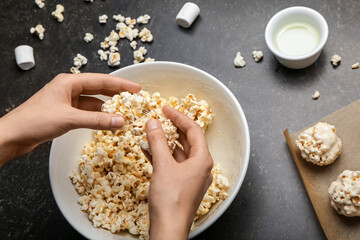 Woman making tasty popcorn balls on dark background