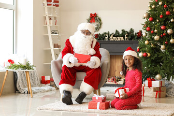 African-American Santa Claus and cute girl with gifts at home on Christmas eve