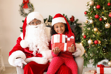 Fototapeta na wymiar African-American Santa Claus and cute girl with gifts at home on Christmas eve