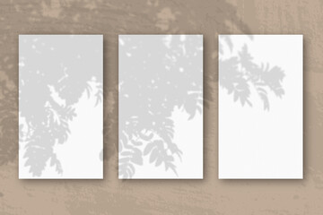 3 vertical sheets of textured white paper on brown table background. Mockup overlay with the plant shadows. Natural light casts shadows from a Rowan branch. Horizontal orientation