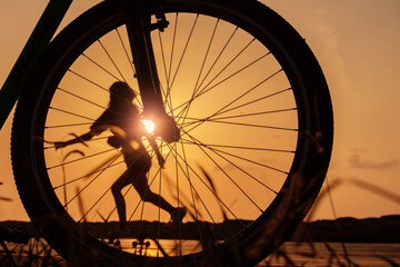 close-up silhouette of a bike wheel at sunset. The sun shines through the wheel of a bicycle with blurred silhouette of skating girl, selective focus