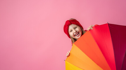 happy little girl looks out from behind an umbrella on a pink background.