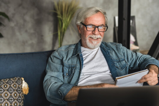 Senior man speak talk on video call while sitting on sofa, elderly professor conduct online lesson using laptop computer
