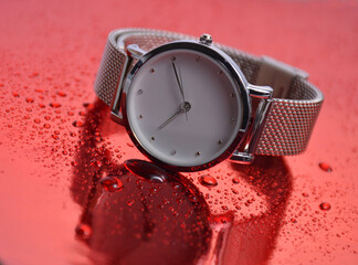 The clock lies on a red background with water drops.