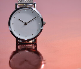 Women's watch on a pink table. Reflection of a clock on a table.