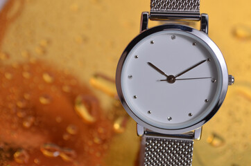 Close-up watch on a golden background. Water drops on the table.