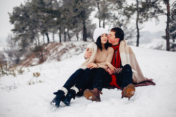 Fototapeta premium Young couple in a winter park. Man with a red sharf. Lady in a red jacket