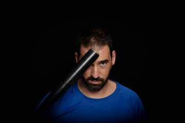 Bearded man dressed in blue t-shirt in defiant pose posing whit a baseball bat on black background