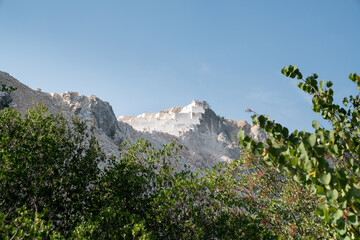 Marble industrial quarry, cutting of white and gray marble in natural environment with rocks, trees and blue sky and leaving their wastes to nature