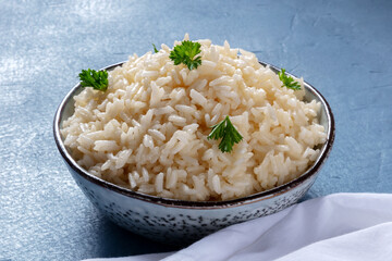 A bowl of white rice, cooked and served with fresh parsley leaves, on a blue background