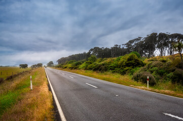 Haast Highway perspective close to Bruce Bay with some increment weather in the distance and the forest line on one side on the western coast of New Zealand at the Tasman Sea.