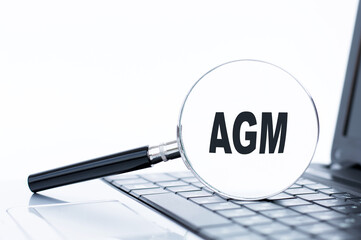 Magnifying glass with text agm on the laptop keyboard, which is on the table. Business concept