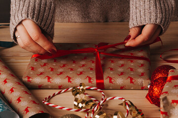 girl in knitted sweater tying a ribbon on a christmas gift.
