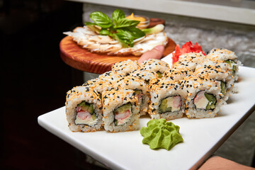 Waiter holds plates with sushi rolls and bacon, onion, mustard. Close-up, selective focus