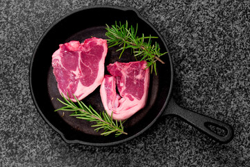 Lamb loin chops with rosemary in a cast iron frying pan.  On a black granite background