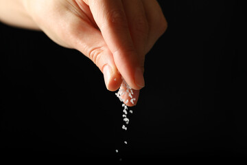 Female hand adding salt on black background