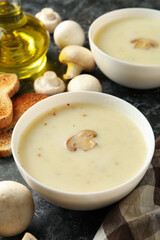 Concept of tasty lunch with bowls of mushroom soup on black smoky background