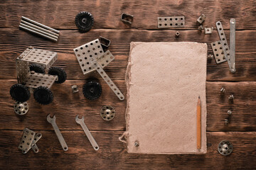 Old retro children metal building kit details in the box and blank instruction book with copy space on the brown wooden table background.