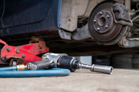 Pneumatic Wrench Tool On The Asphalt And A Car Jack For Lift Up The Body And Changing The Tire. Car Without Wheel.