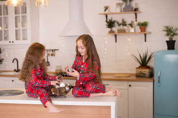 Two little girls in same pajamas in the kitchen playing with christmas toys in christmas morning....