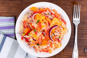 Traditional Mediterranean salad of couscous, tomato, pepper and onion in a plate on a wooden table, close-up, top view - Moroccan and Algerian cuisine