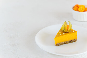 Slice of pumpkin cheesecake with physalis on a white plate. Horizontal orientation, copy space.