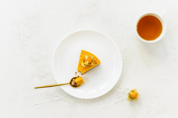 A slice of pumpkin cheesecake with physalis on a white plate with a cup of tea. Horizontal orientation, top view.