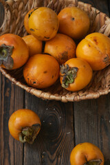 basket with a harvest of persimmons on a wooden table. Country style