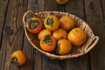 basket with a harvest of persimmons on a wooden table. Country style