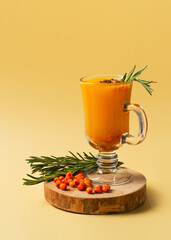 Sea buckthorn drink with rosemary in glass on yellow background