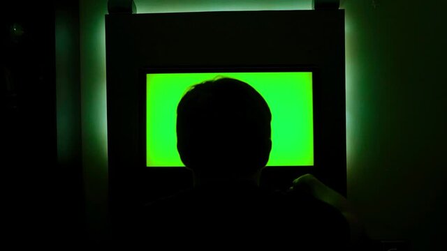 Rear view of man looking at green TV. Concept. Man was watching green-screen TV sitting in dark. Man turned off TV and went to sleep