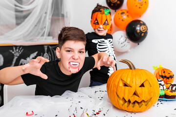 Scary boy with vampire fangs looking at the camera on thehalloween party. Jack O' Lantern Halloween pumpkin on the table