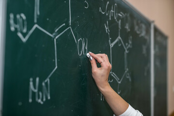 female hand draws chemical equations on a blackboard