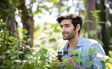 Young handsome man looking natural and using binoculars in public park with a happy face standing and smiling. Concept of nature and wildlife studies.