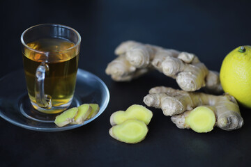 Ginger root whole and sliced. Ginger tea with lemon on the dark background. Fresh ginger root on stone background. Vitamins. Free space for your text.