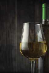 Transparent bottle of white dry wine on the table. White wine glass on a wooden background.