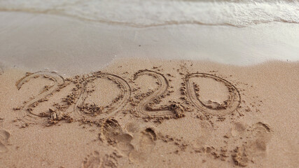 Numbers 2020 year on the sea shore, wave covering lettering. Concept of end awful year