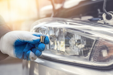 Repairment holding new car light bulb under deception for headlamp, car as background