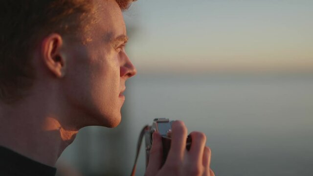 Close up profile of young male photographer taking outdoor photo at sunset
