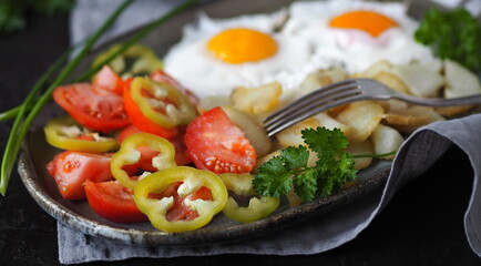 Fried eggs with potatoes, tomatoes and herbs on an exotic plate on a dark background.Healthy breakfast made from natural products.