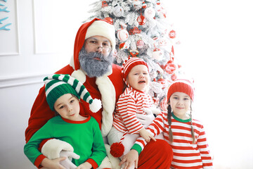 Fototapeta premium Santa Claus sitting with little cute elves over Christmas background. Time of miracles. Gifts from Santa Claus.