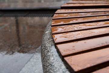 One of the circle benches on the Griboyedov channel embankment in Saint Petersburg on a rainy autumn day in October. Wet wooden planks are laid on a granite pedestal. Copy space